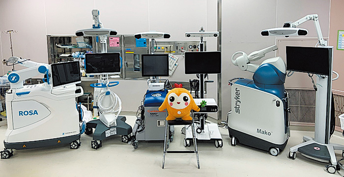 患者の容態、使用する人工関節の機種に合わせて、3種類の手術支援ロボットの中から最適なものを選択し、活用している。中央は医療生協さいたまマスコットのココロン