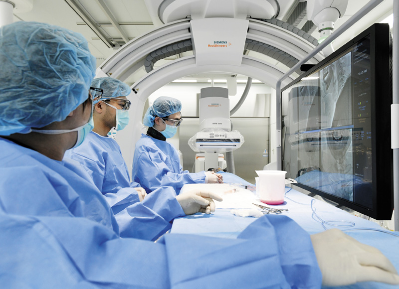 CTや血管撮影装置も新しい機種を導入しており、繊細な血管内治療に活かされている。写真は奥から、恩田医師→髙橋医師→倉内医師（脳神経内科医）