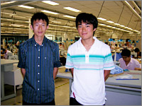 縫製現場を背景に撮影してもらった。たくさんの工員さんが熱心にミシンがけをしていた